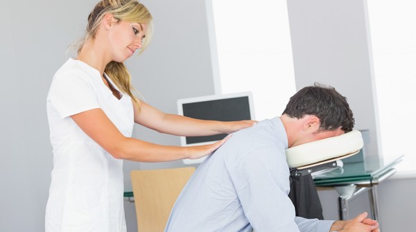 Masseuse treating clients shoulder in massage chair