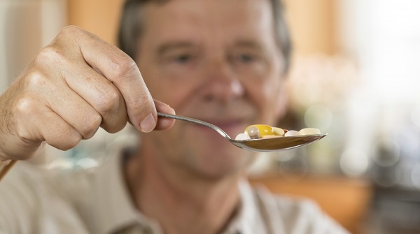 Senior man eating a spoon of vitamins